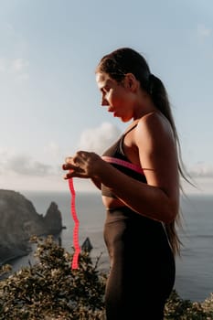 A woman is holding a pink tape measure and is measuring her breasts. The tape measure is marked with numbers, and the woman is looking at it intently