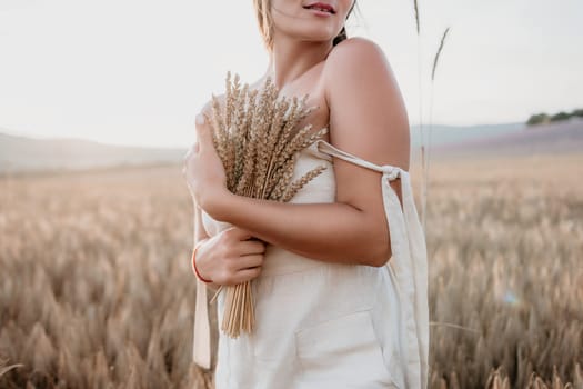 A woman is holding a bunch of wheat in her arms. The wheat is dry and brown, and the woman is wearing a white dress. The scene is set in a field, and the woman is posing for a photo