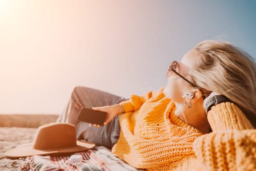 A woman in a yellow sweater lies on a blanket in a field, enjoying the sunshine.