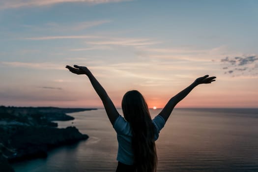 A woman stands with open arms, her silhouette outlined against a vibrant sunset over the ocean.