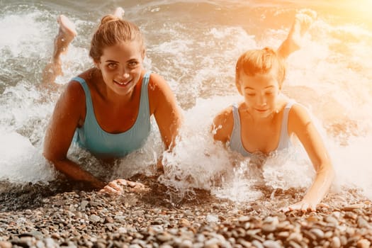 A mother and her daughter are playing in the foamy water on a pebble beach.