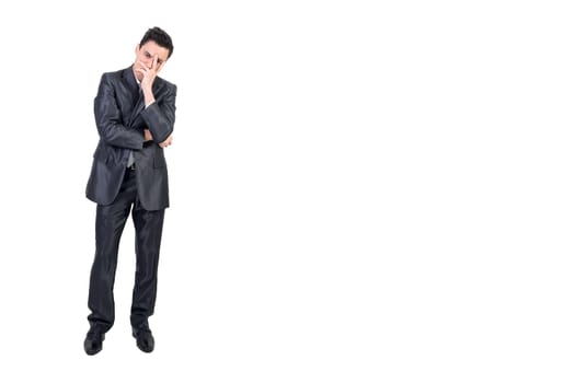 Full length of bored young male entrepreneur with dark hair in formal suit covering face with hand and looking at camera against white background