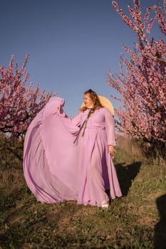 Woman blooming peach orchard. Against the backdrop of a picturesque peach orchard, a woman in a long pink dress and hat enjoys a peaceful walk in the park, surrounded by the beauty of nature