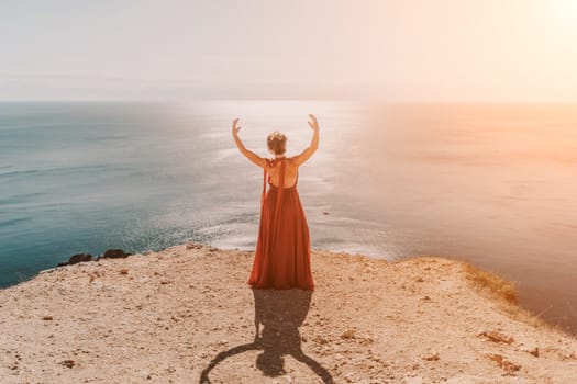 Woman red dress sea. Female dancer in a long red dress posing on a beach with rocks on sunny day. Girl on the nature on blue sky background