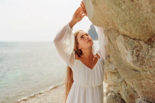 woman white dress standing on a beach, looking out at the ocean. She is lost in thought, with her hand on her hip. Concept of calm and introspection