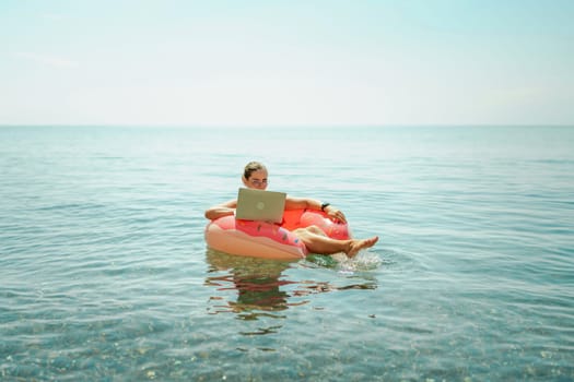 Woman laptop sea. Freelancer woman in sunglases floating on an inflatable big pink donut with a laptop in the sea. People summer vacation rest lifestyle concept