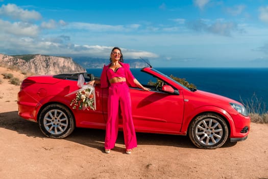 A woman stands in front of a red convertible car, holding a bouquet of flowers. Concept of freedom and adventure, as the woman is dressed in a red outfit and poses in front of the car