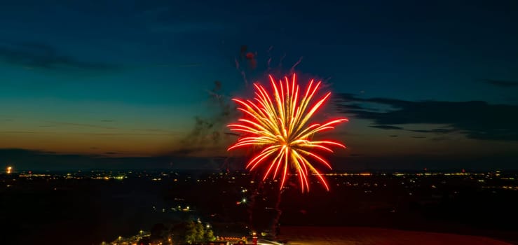 Red And Gold Fireworks Exploding In The Night Sky, Creating Bright Bursts Over The Distant City Lights And A Gathered Crowd, With A Twilight Horizon Enhancing The Festive Scene.