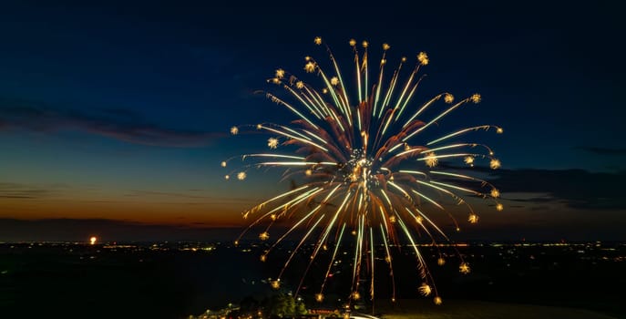 Green And Gold Fireworks Exploding In The Night Sky, Creating Stunning Bursts Over The Distant Cityscape And A Gathered Crowd, With A Vibrant Twilight Horizon Enhancing The Festive Atmosphere.