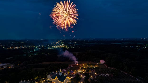 Golden Fireworks Burst Against The Night Sky, Illuminating A Rural Fairground With White Barns And Small Churches, While The Glow Of Distant City Lights Enhances The Festive Atmosphere.
