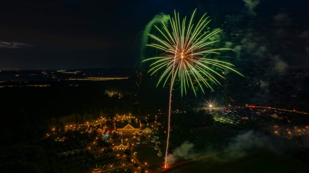 Brilliant Green Fireworks Burst Over A Well-Lit Estate, Surrounded By Trees And Fields, With Distant City Lights Adding Depth To The Festive Nighttime Scene.