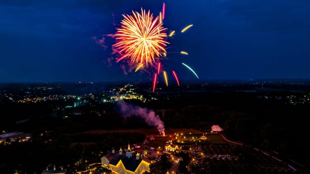 Brilliant Red And Gold Fireworks Light Up The Night Sky Over A Picturesque Rural Fairground With White Barns And Small Churches, Creating A Festive And Vibrant Atmosphere Against The Dark Backdrop.