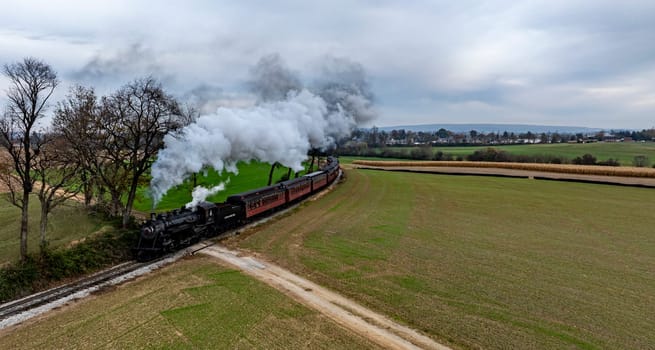 Ronks, Pennsylvania, USA, October 4, 2023 - A vintage steam train winds through a green field, releasing smoke against a backdrop of overcast skies.