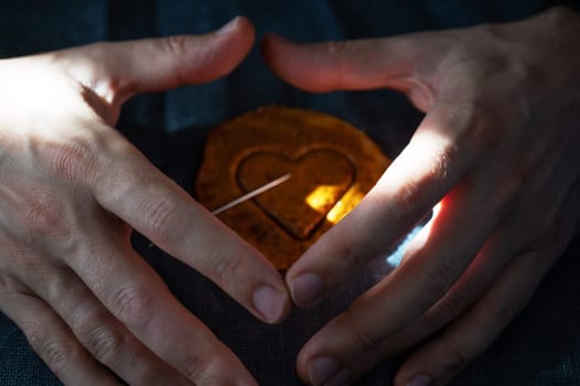 Men's hands closeup with brown sugar caramel candy cookies with a metal needle in the shape of a heart. Concept of survival game