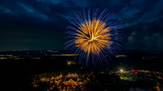 Golden And Blue Fireworks Burst Over A Well-Lit Estate, Surrounded By Trees And Fields, With Distant City Lights Adding Depth To The Festive Nighttime Scene.
