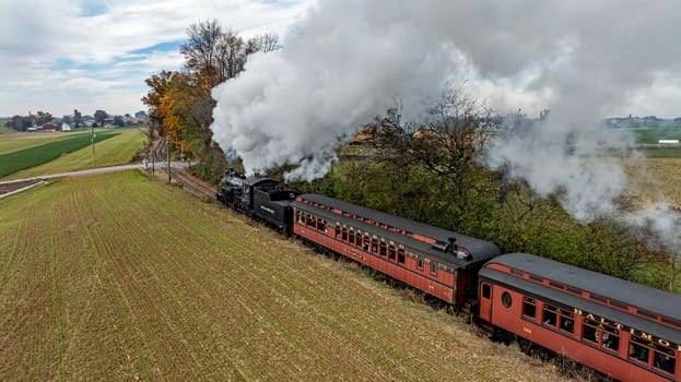 Ronks, Pennsylvania, USA, October 4, 2023 - A steam train chugs along a rural track, billowing smoke against a backdrop of fields and trees in autumn.