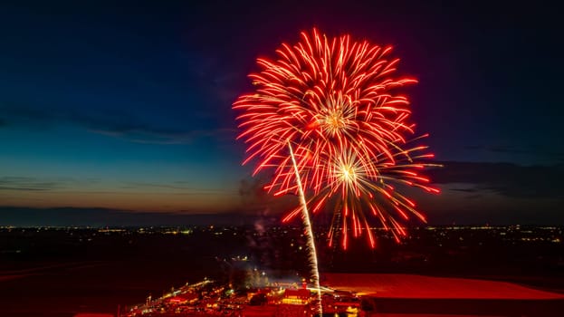 Bright Red Fireworks Exploding In The Night Sky, Creating Brilliant Bursts Over The Distant City Lights And A Gathered Crowd, With The Twilight Horizon Adding To The Festive Atmosphere.