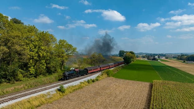 A vintage steam train moves along tracks surrounded by vibrant fields and trees on a sunny day. High quality photo