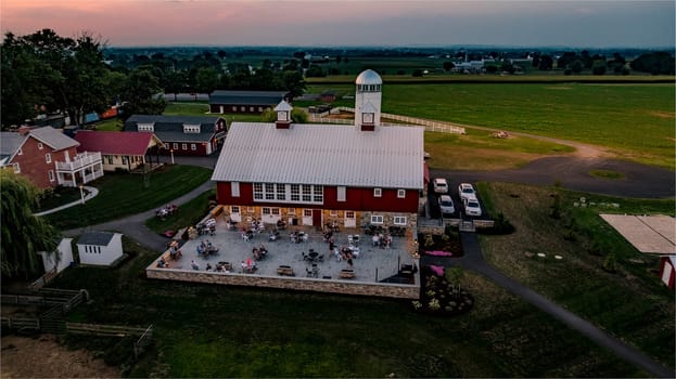 Ronks, Pennsylvania, USA, August 1, 2024 - People enjoy an outdoor gathering at a barn venue surrounded by green fields during sunset.