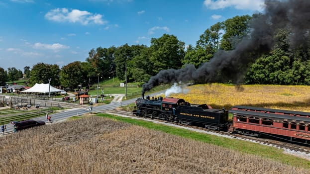 Ronks, Pennsylvania, USA, October 4, 2023 - A steam engine pulls a vintage train past a cornfield and fairground under a clear blue sky.