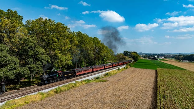 Ronks, Pennsylvania, USA, October 4, 2023 - A vintage steam train moves along tracks surrounded by vibrant fields and trees on a sunny day.