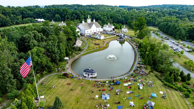 Elizabethtown, Pennsylvania, USA, July 4, 2024 - Charming Rural Fairground With A Serene Pond, White Barns, Small Churches, And People Enjoying Festivities, Surrounded By Green Trees And Rolling Hills, Creating A Vibrant Community Atmosphere.