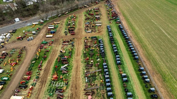 Aerial View Of Multiple Rows Of Horse-Drawn Buggies And Extensive Array Of Colorful Farming Equipment On A Green And Brown Field, Showcasing A Rural Agricultural Setup With Various Tools.