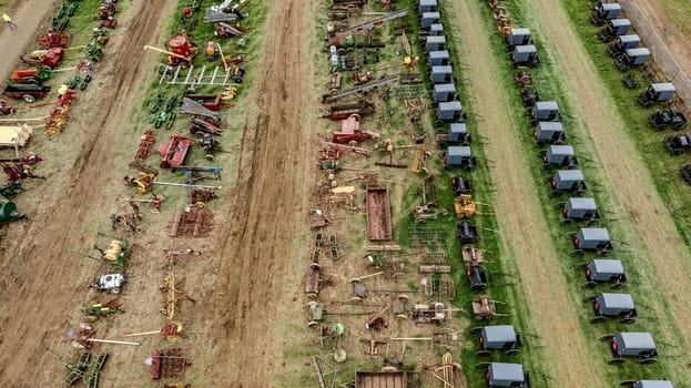 Aerial View Of Multiple Rows Of Horse-Drawn Buggies And Extensive Array Of Colorful Farming Equipment On A Green And Brown Field, Showcasing A Rural Agricultural Setup With Various Tools.