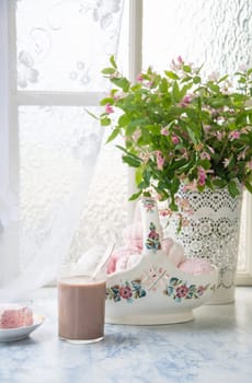 delicate still life with a full vase of vanilla marshmallows and a glass of coffee with milk, next to a vase with lilac branches on a wooden table, emphasizing the floral and rustic lifestyle,