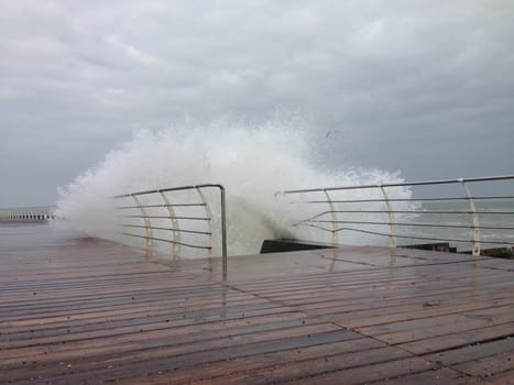 Stormy waves splashing on the wooden decked promenade. High quality photo