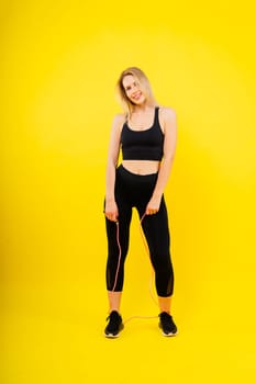 Fitness woman doing jumping exercises with a skipping rope on colorful yellow background.