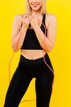 Fitness woman doing jumping exercises with a skipping rope on colorful yellow background.