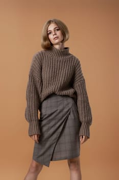 beautiful blonde woman in brown knitted sweater posing on beige background. autumn style