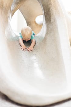 Child playing on outdoor playground. Toddler plays on school or kindergarten yard. Active kid on stone sculpured slide. Healthy summer activity for children. Little boy climbing outdoors