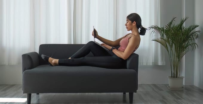 Girl in sports bar outfit Relaxing using the laptop on the living room sofa..