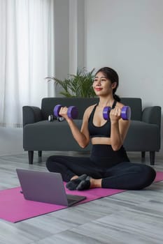 Young woman exercising in front of laptop Wear a sports bar outfit. Do yoga and lift dumbbells on the exercise mat..