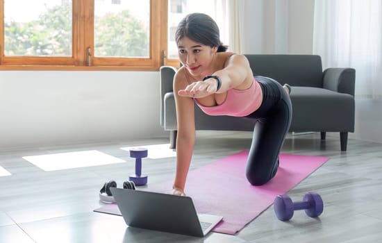 Young woman exercising in front of laptop Wear a sports bar outfit. Do yoga and lift dumbbells on the exercise mat..