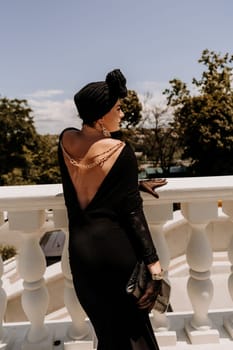 Stylish woman in the city. Fashion photo of a beautiful model in an elegant black dress posing against the backdrop of a building on a city street.