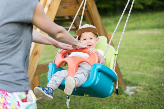 Mother pushing her infant baby boy child on a swing on playground outdoors