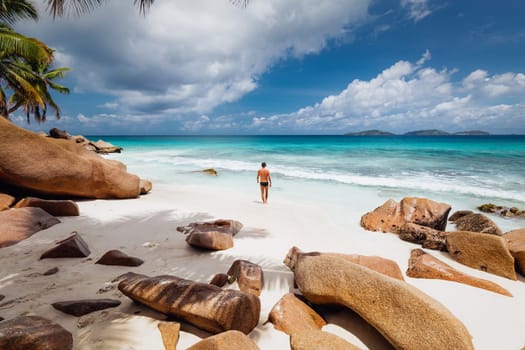 Active sporty man wearing black swimsuit enjoying swimming and snorkeling at amazing on Anse Patates beach on La Digue Island, Seychelles. Summer vacations on picture perfect tropical beach concept.
