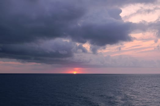 Sunset over the mediterranean sea on a cloudy day.Ocean, rain clouds, horizon line, empty space with no one, cold tones, blue, orange sunshine