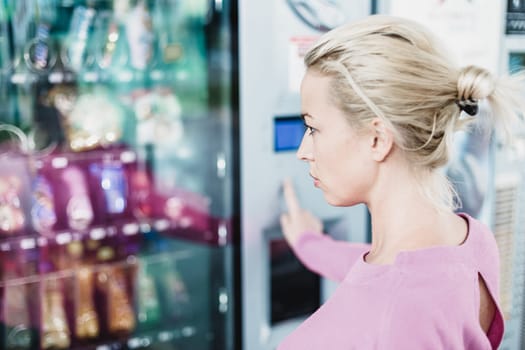 Caucasian woman using a modern vending machine. Her right hand is placed on the dia pad.