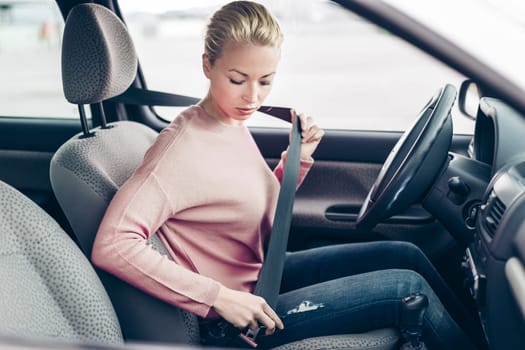 Safety first. Beautiful blonde caucasian lady fastening car seat belt.