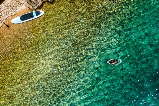 Woman swimming in clean, shallow sea water after SUP session.