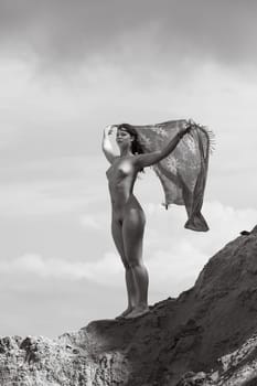 Young woman posing nude and enjoying nature on sand hill against sky background. Nature, beauty and nudity concept