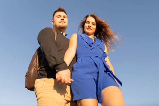 Young couple holding hands is standing under a blue sky on a sunny summer day