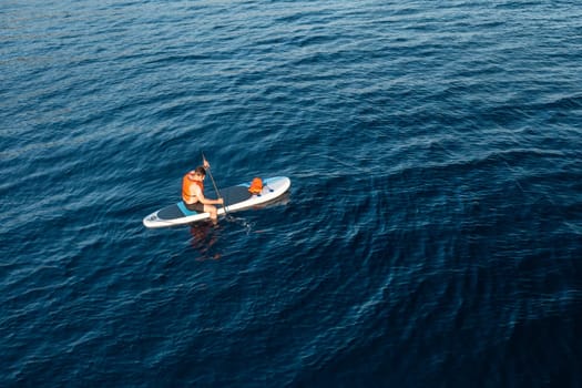 A male tourist, surrounded by the breathtaking blue of the azure sea, paddles effortlessly on a board