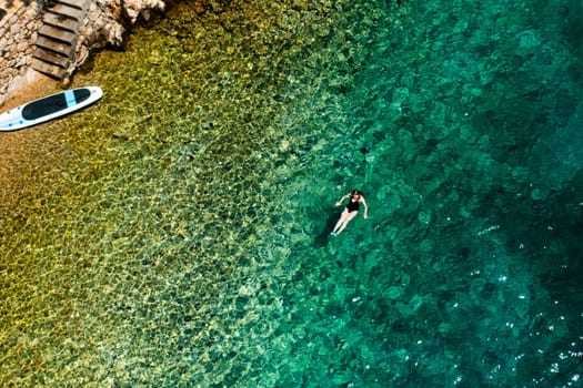 Woman swimming on the back in crystal clear water and paddle board is on the seaside.