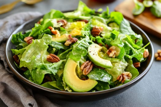 Healthy green salad with sliced avocado, mixed greens, and crunchy nuts served in a dark bowl.