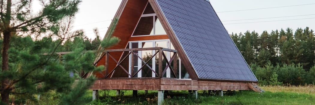 The concept of glamping and renting a chalet for weekend. Wooden house with a veranda in nature around coniferous trees.